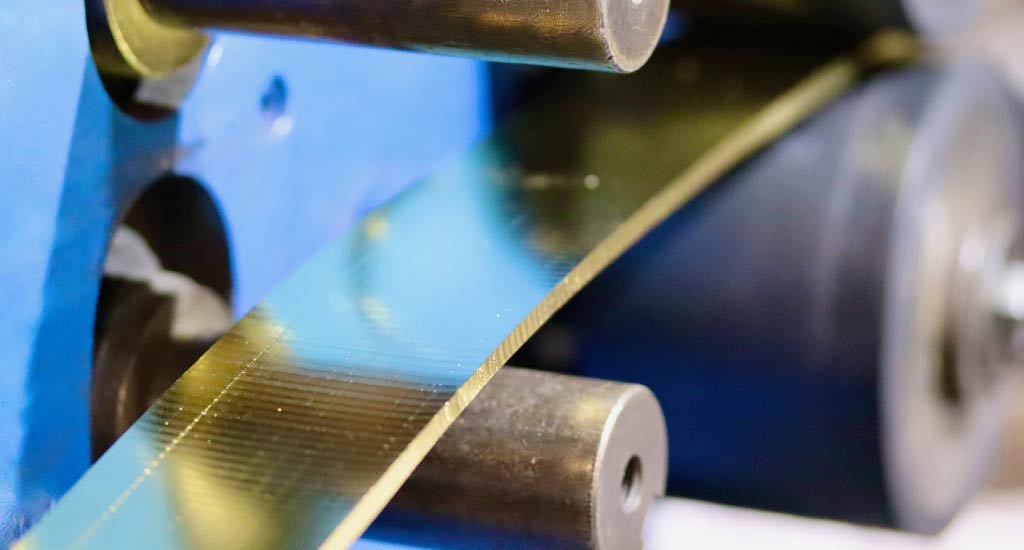Gold material being rolled through a rolling mill for precision manufacturing.